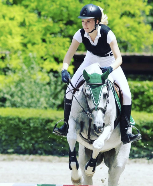 Amazzone su cavallo grigio durante un salto ostacoli